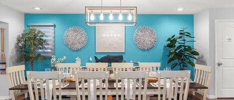 A dining area with a round table, white chairs, a blue accent wall, and decorative wall art.