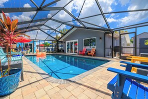A swimming pool with a glass enclosure, surrounded by lounge chairs and a covered patio area. - Flamingo Palms | 6BR Estate · Heated Pool · Game Room · Sleeps 10 (Seminole)