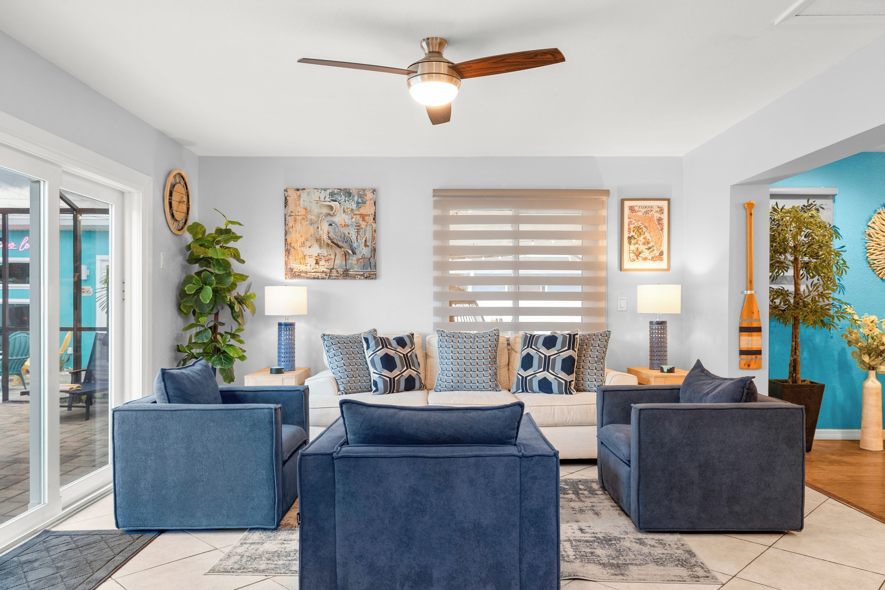 A modern living room with a ceiling fan, a large window with blinds, a sofa set, and a potted plant.