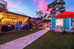 A patio area with outdoor seating, a barbecue grill, and a small blue structure with a red umbrella.