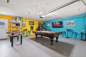 Una habitación con mesa de billar, mesa de fútbol de mesa y un cartel de Harley-Davidson en la pared.