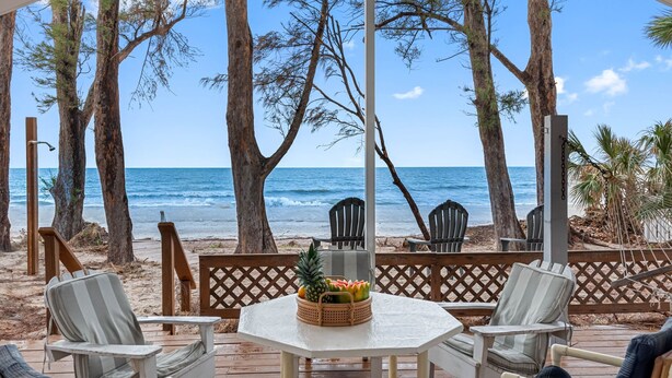 Un patio frente a la playa con una mesa, sillas y una cesta de frutas.