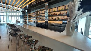 Una zona de bar con una barra alargada, estantes con varias botellas y un jarrón decorativo.