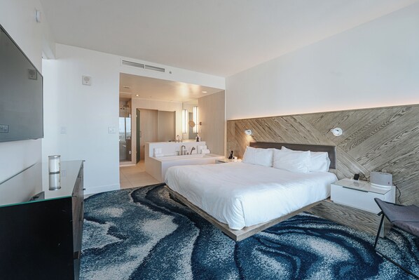 A modern hotel room with a large bed, a separate bathroom, a flat-screen TV, and a desk with a chair.