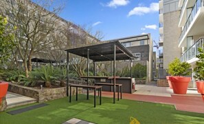 Een terras buiten met een pergola, banken en planten in potten.