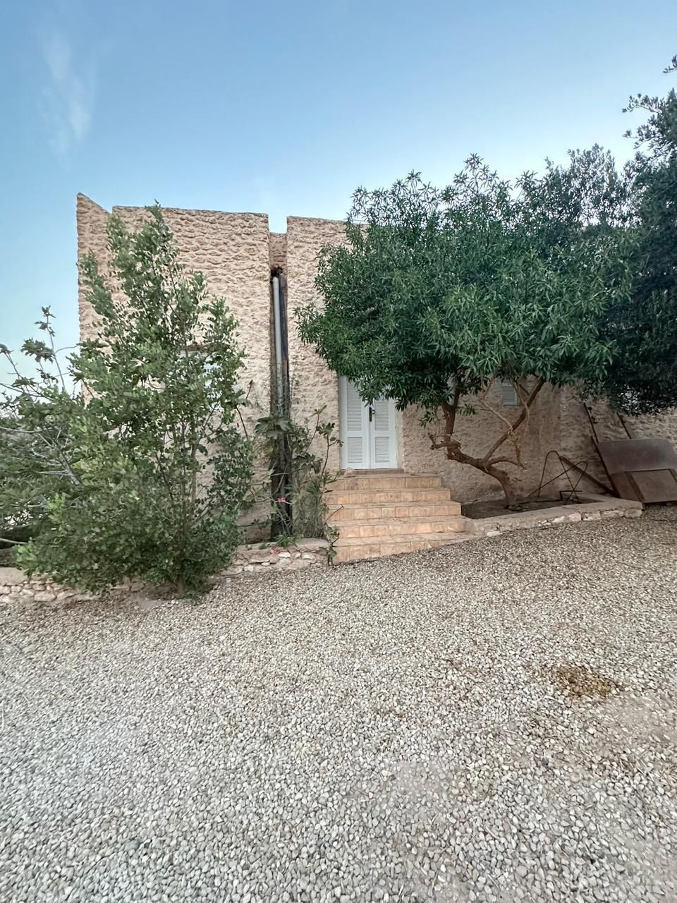 A building with a stone facade, a small entrance with steps, and a gravel driveway.