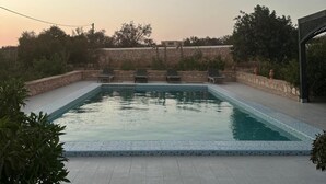 Ein rechteckiger Pool mit gefliestem Sonnendeck, umgeben von Steinmauern und Grünpflanzen.
