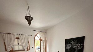 Ein Schlafzimmer mit einem großen Bett, einem kleineren Bett, einer Chandelüster, einem Gemälde und Blick durch eine offene Tür.