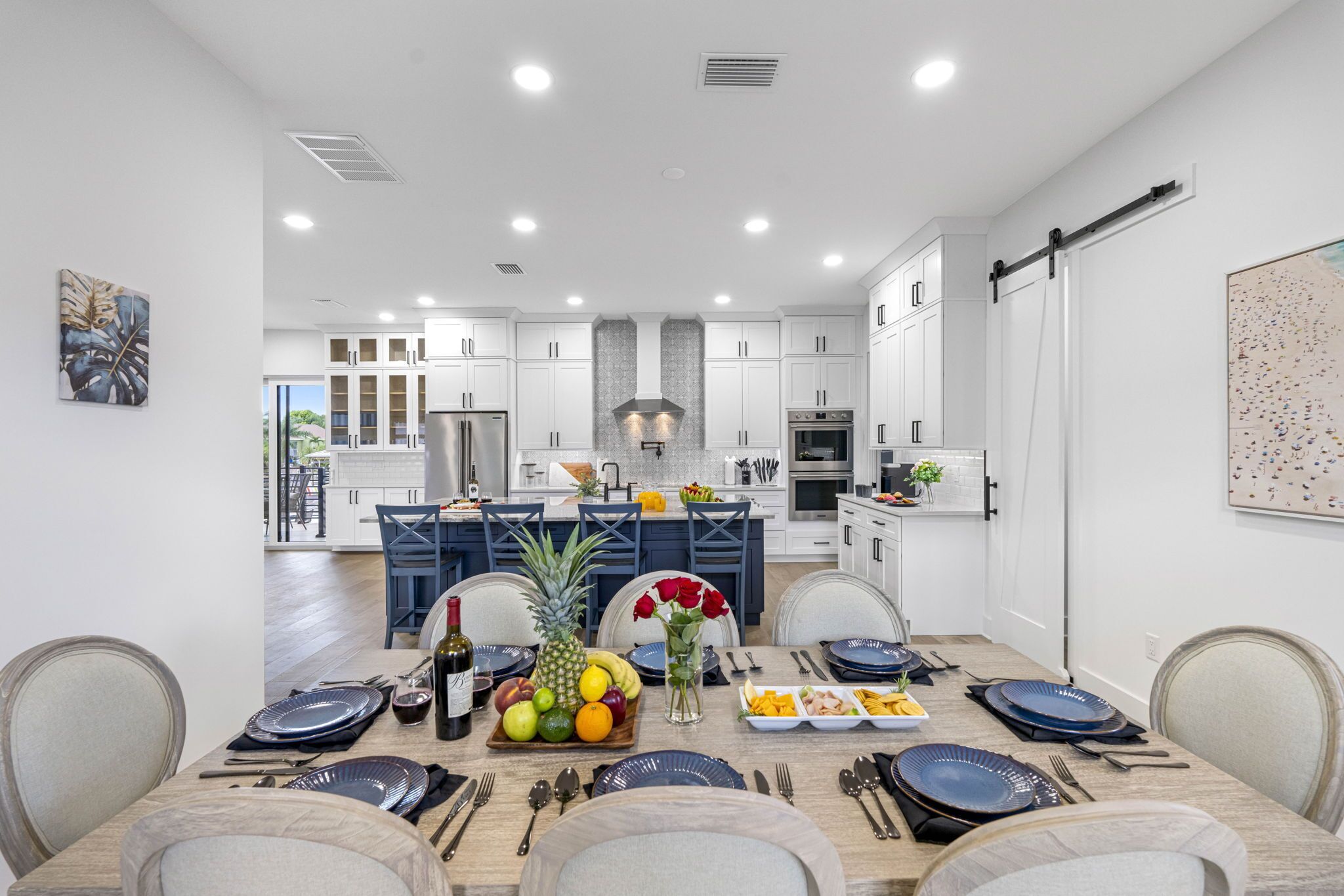 A modern kitchen with white cabinets, a central island, and a dining area set for six.