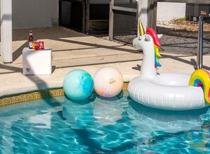 Une piscine avec des bouées en forme de licorne gonflable et une glacière blanche remplie de boissons.