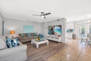 A modern living room with a flat-screen TV, a ceiling fan, a sofa, and a coffee table. - Screened Heated Pool, 15 Min to Beach | 4BR Sleeps 10, Largo (Largo)