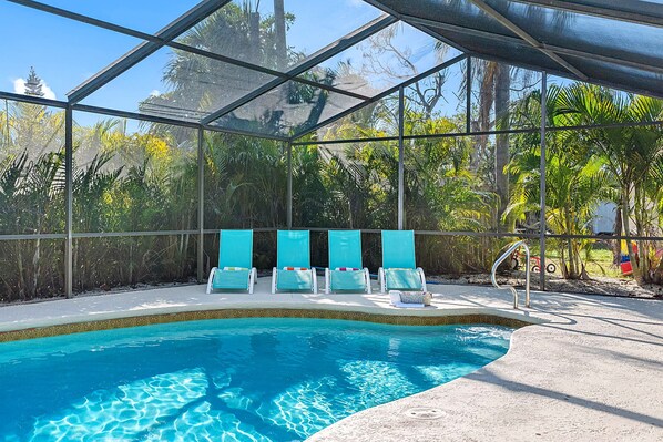 An indoor swimming pool with clear blue water, surrounded by a glass enclosure, and four lounge chairs with cushions.