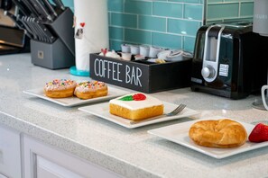 Een aanrecht met een koffiebarbordje, een broodrooster en diverse ontbijtartikelen, zoals donuts en een croissant.