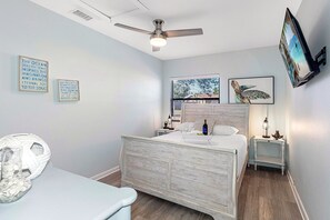 A bedroom with a bed, a ceiling fan, a window with a view, a bedside table with a lamp, and wall art. - Screened Heated Pool, 15 Min to Beach | 4BR Sleeps 10, Largo (Largo)