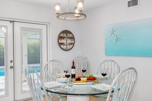 A dining area with a glass table, white chairs, a chandelier, a clock, and a painting of stars. - Screened Heated Pool, 15 Min to Beach | 4BR Sleeps 10, Largo (Largo)