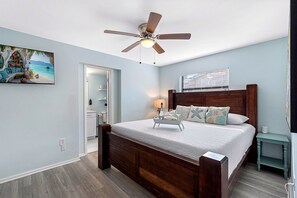 Een slaapkamer met een houten bed, een plafondventilator, een nachtkastje en een raam met jaloezieën.