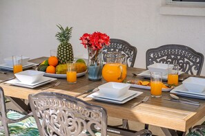 A breakfast table set with plates, bowls, a pineapple, a pitcher of orange juice, and a vase with red flowers. - Screened Heated Pool, 15 Min to Beach | 4BR Sleeps 10, Largo (Largo)