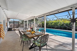A covered outdoor dining area with a pool in the background. - Screened Heated Pool, 15 Min to Beach | 4BR Sleeps 10, Largo (Largo)