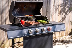 Een kolengrill met vier branders, een opklapbaar bijzettafeltje en een deksel.