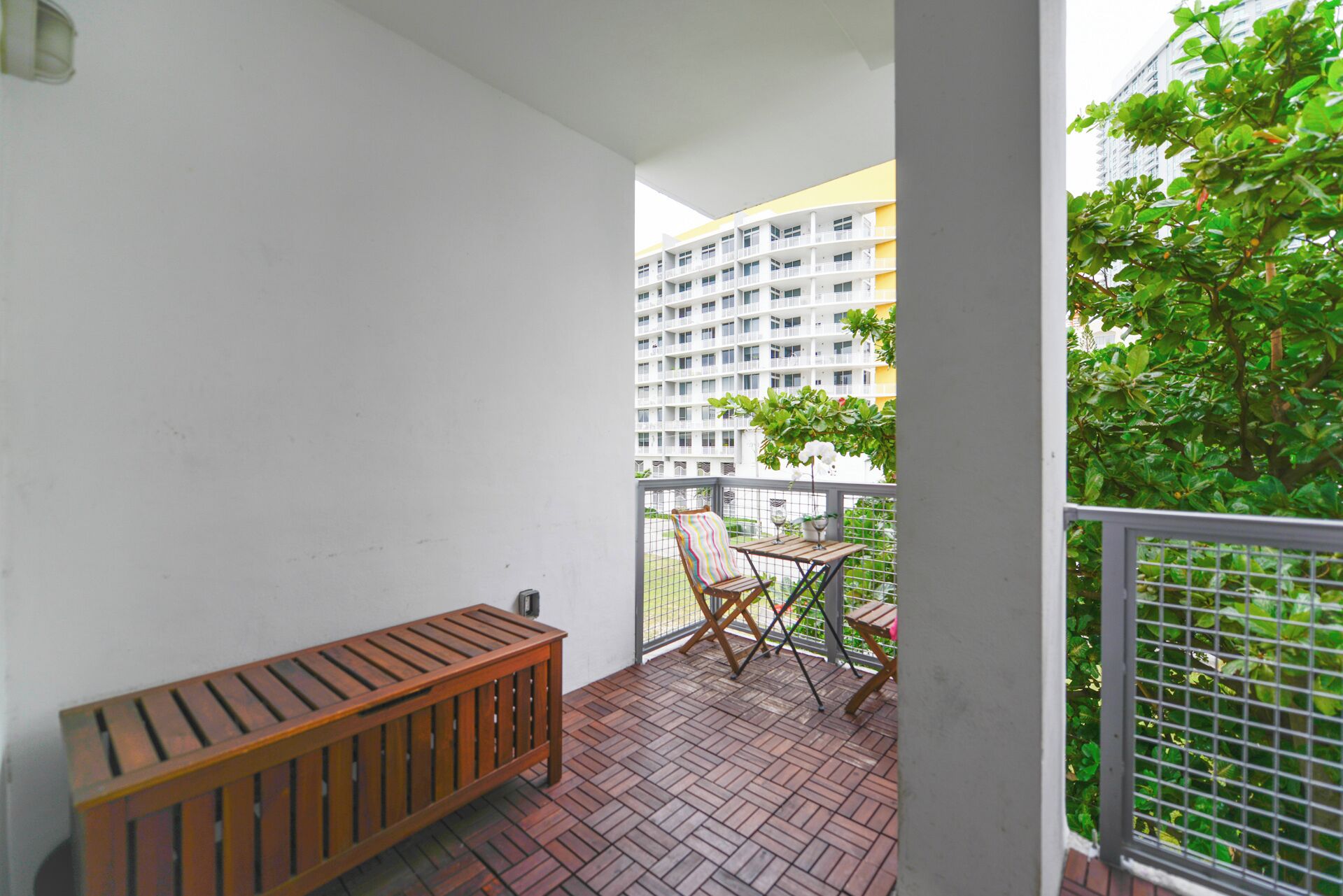 A balcony with a wooden bench, a small table, and a chair with a striped cushion.
