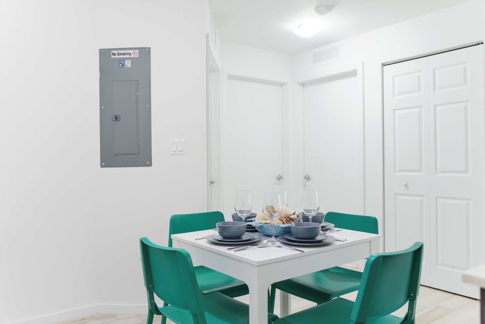 A dining area with a white table set for four, green chairs, and a 'No Smoking' sign on the wall.