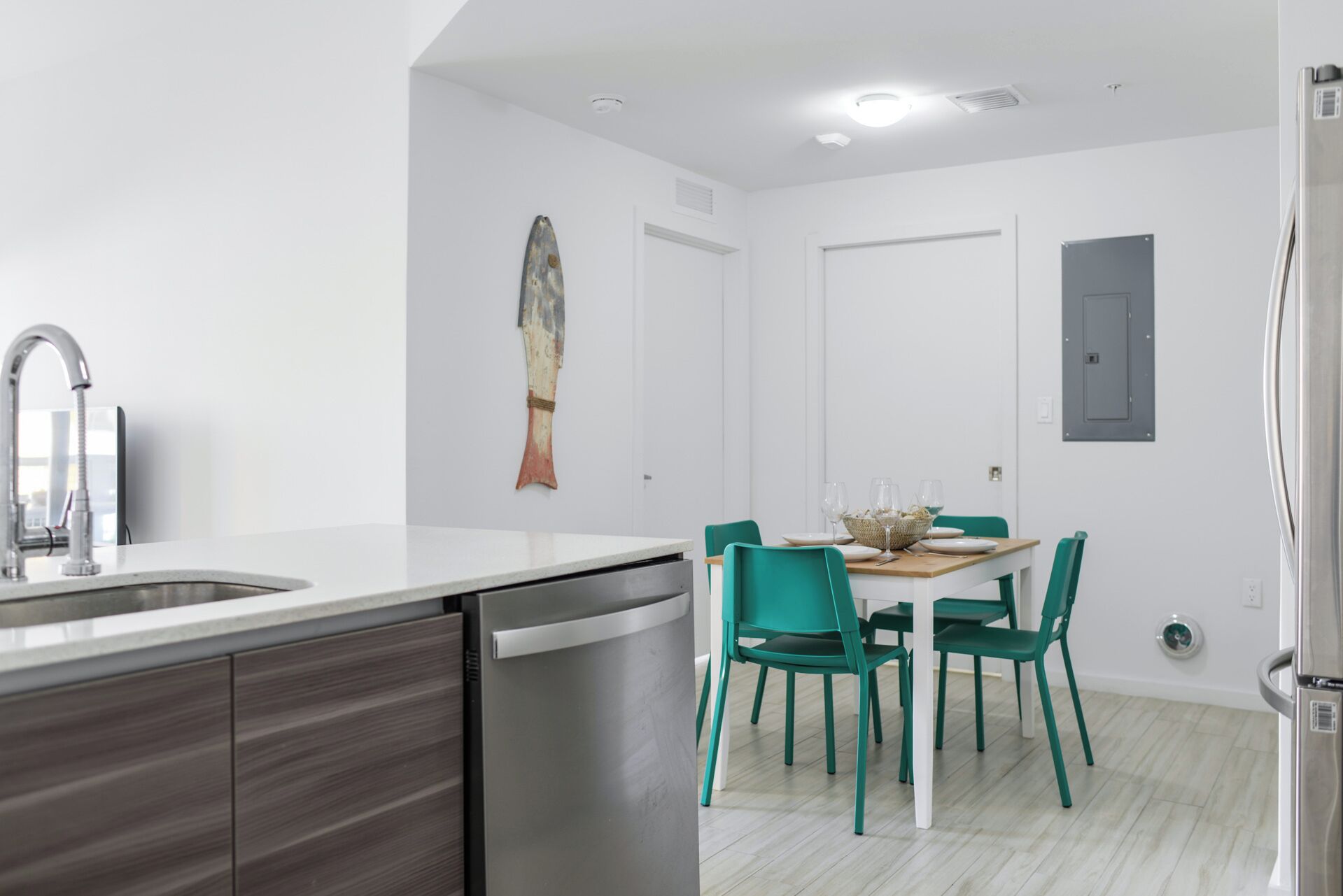 A modern kitchen with a dishwasher, a dining table with chairs, and a wall-mounted light fixture.