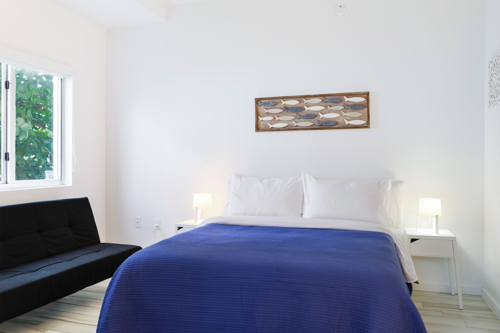 Quarto com cama, duas luminárias de cabeceira, janela e uma obra de arte na parede.