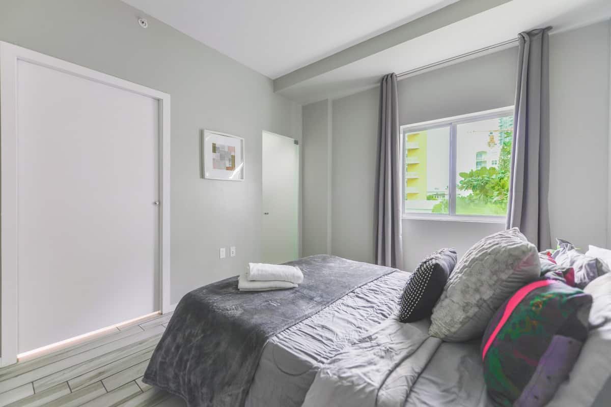 Une chambre à coucher avec un lit, une fenêtre avec des rideaux, une porte et un tableau accroché au mur.