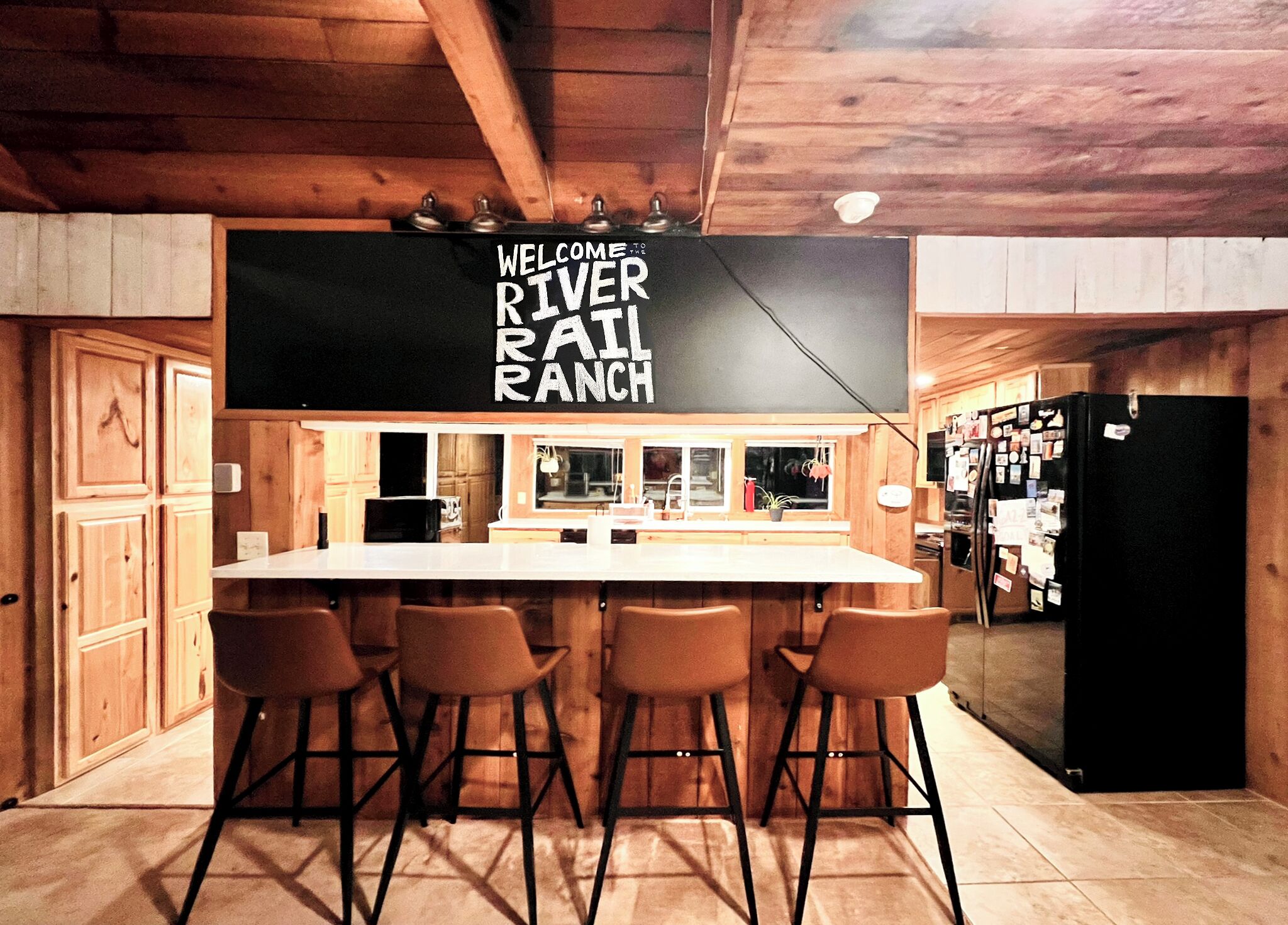 Een rustieke keuken met een bar, houten kasten en een schoolbord waarop staat: 'WELCOME TO RIVER RANCH'.