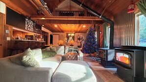 Ein gemütliches Blockhaus-Interieur mit Kamin, Weihnachtstannenbaum und rustikaler Holzbalkendecke.