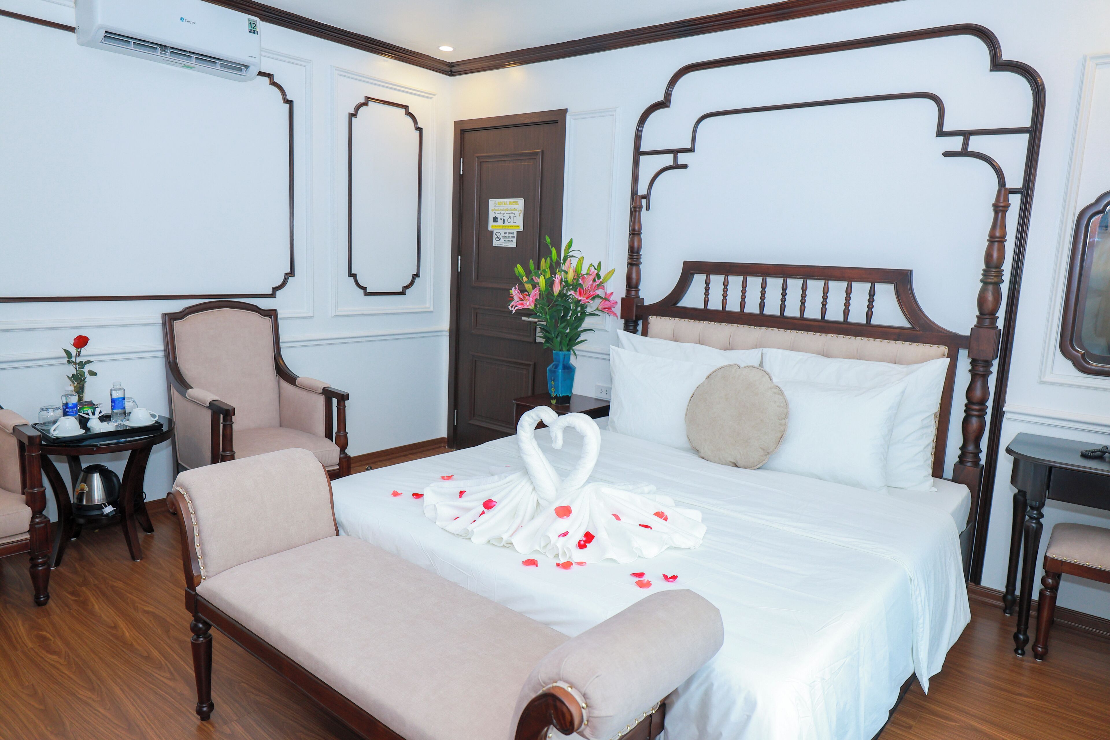 Ein Hotelzimmer mit einem hölzernen Himmelbett, einer Bank, einem kleinen Tisch mit Blumenvase und einem Sessel.