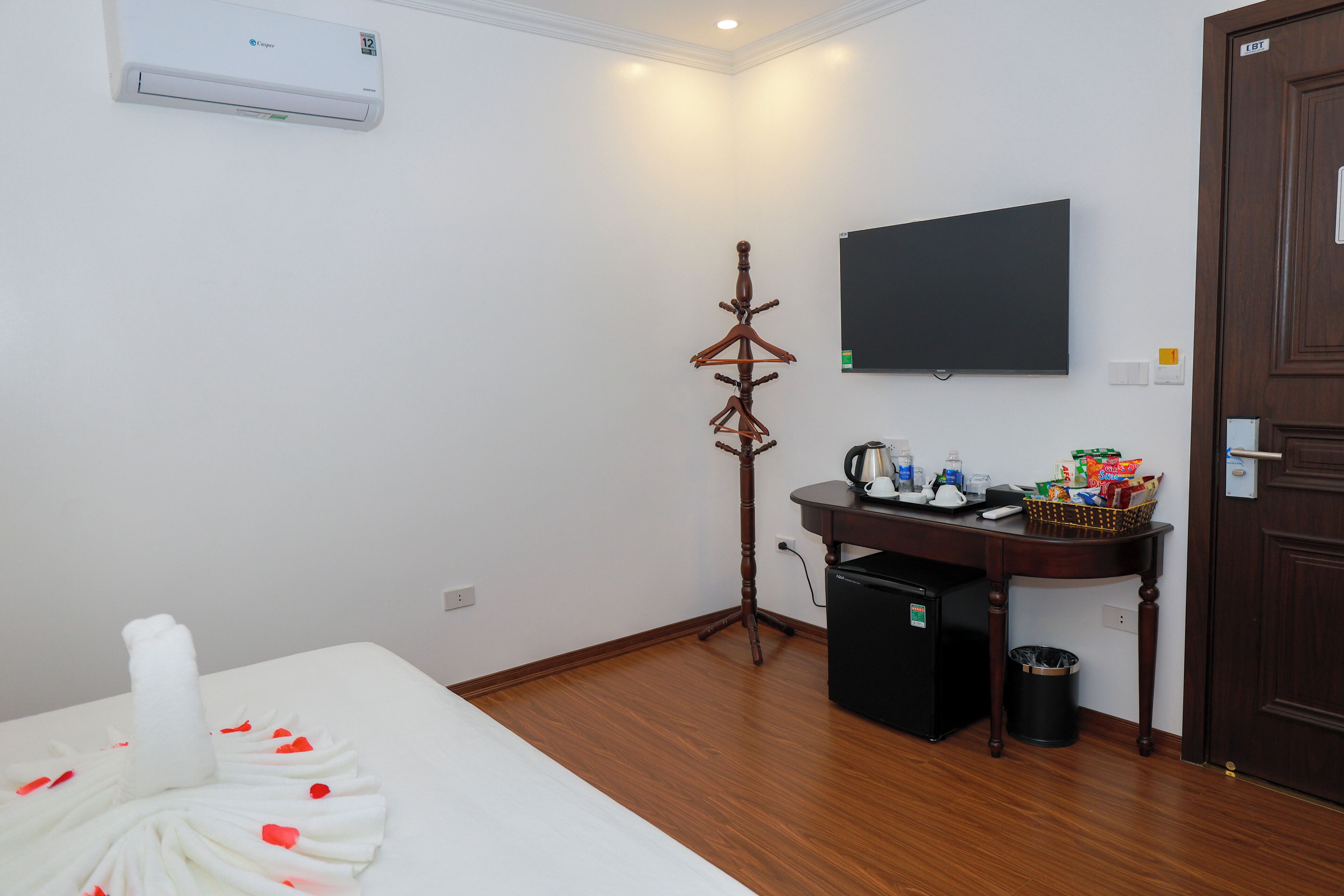 A hotel room with a bed, a small table with a basket, a TV, a heater, and a trash bin.
