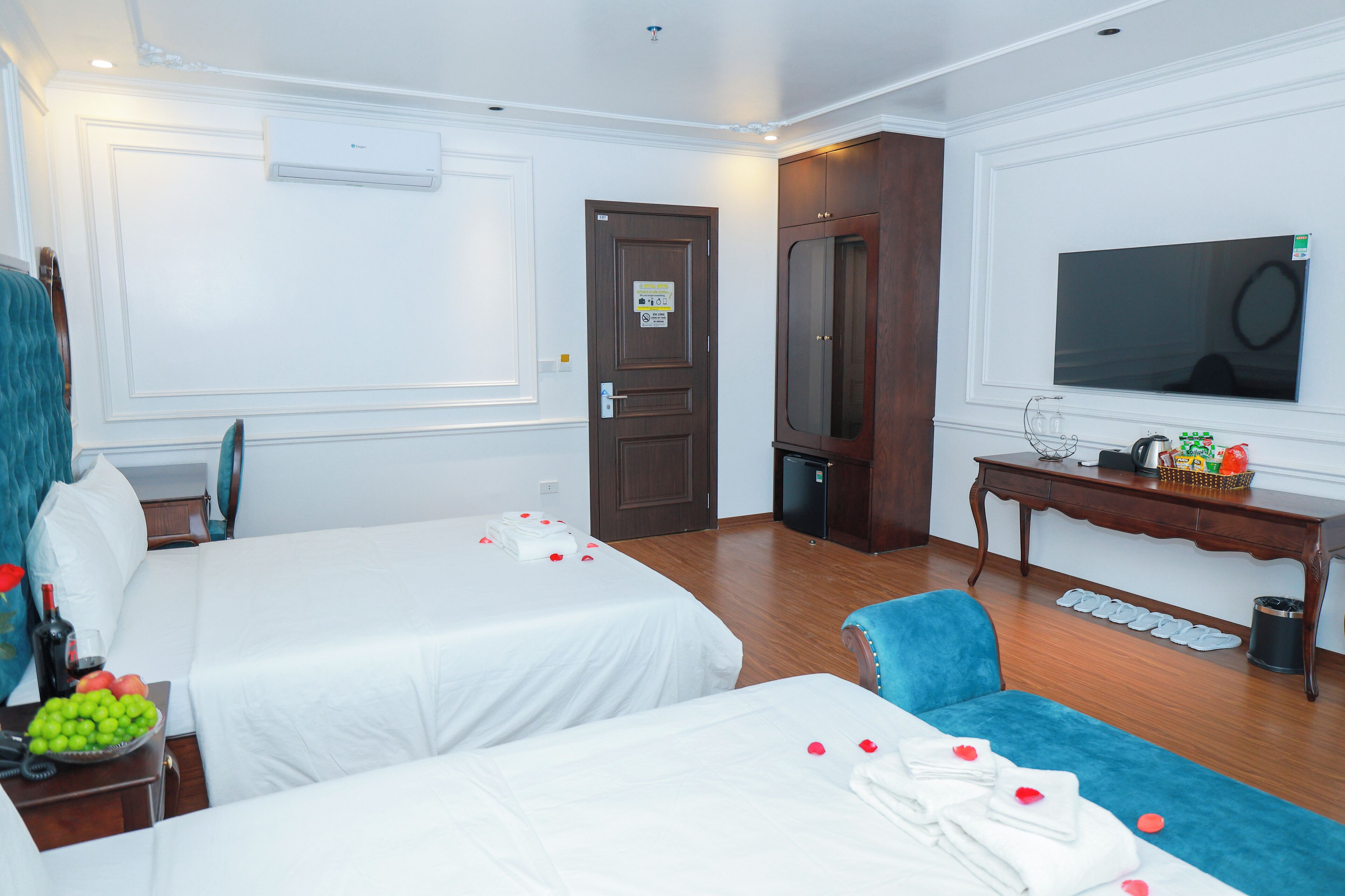 A hotel room with two beds, a TV, a desk, and a small fridge.