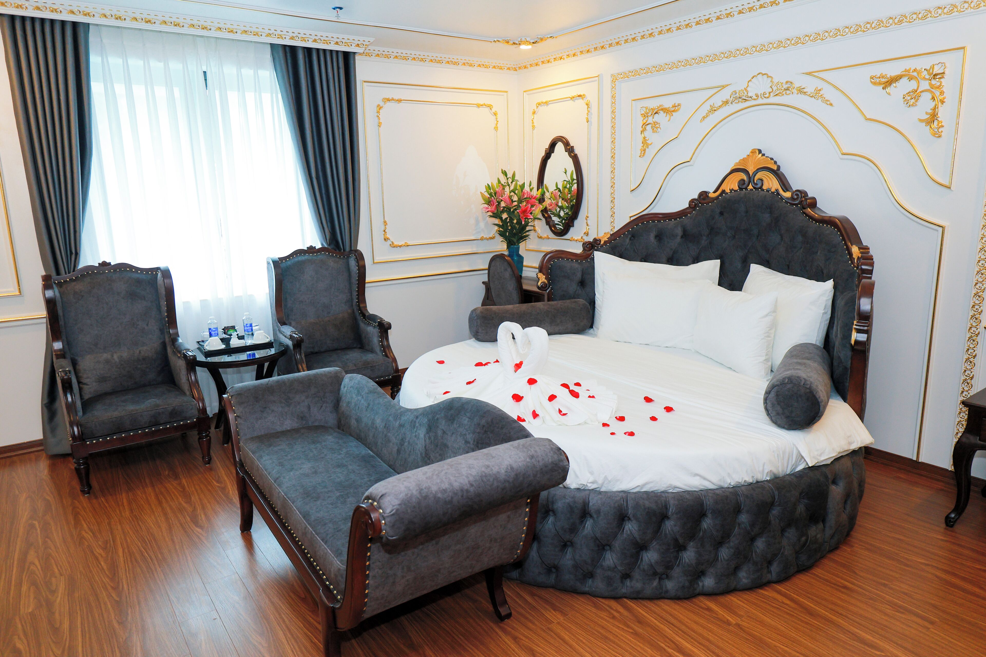 A luxurious bedroom with a large bed, two armchairs, a small table, and a mirror.
