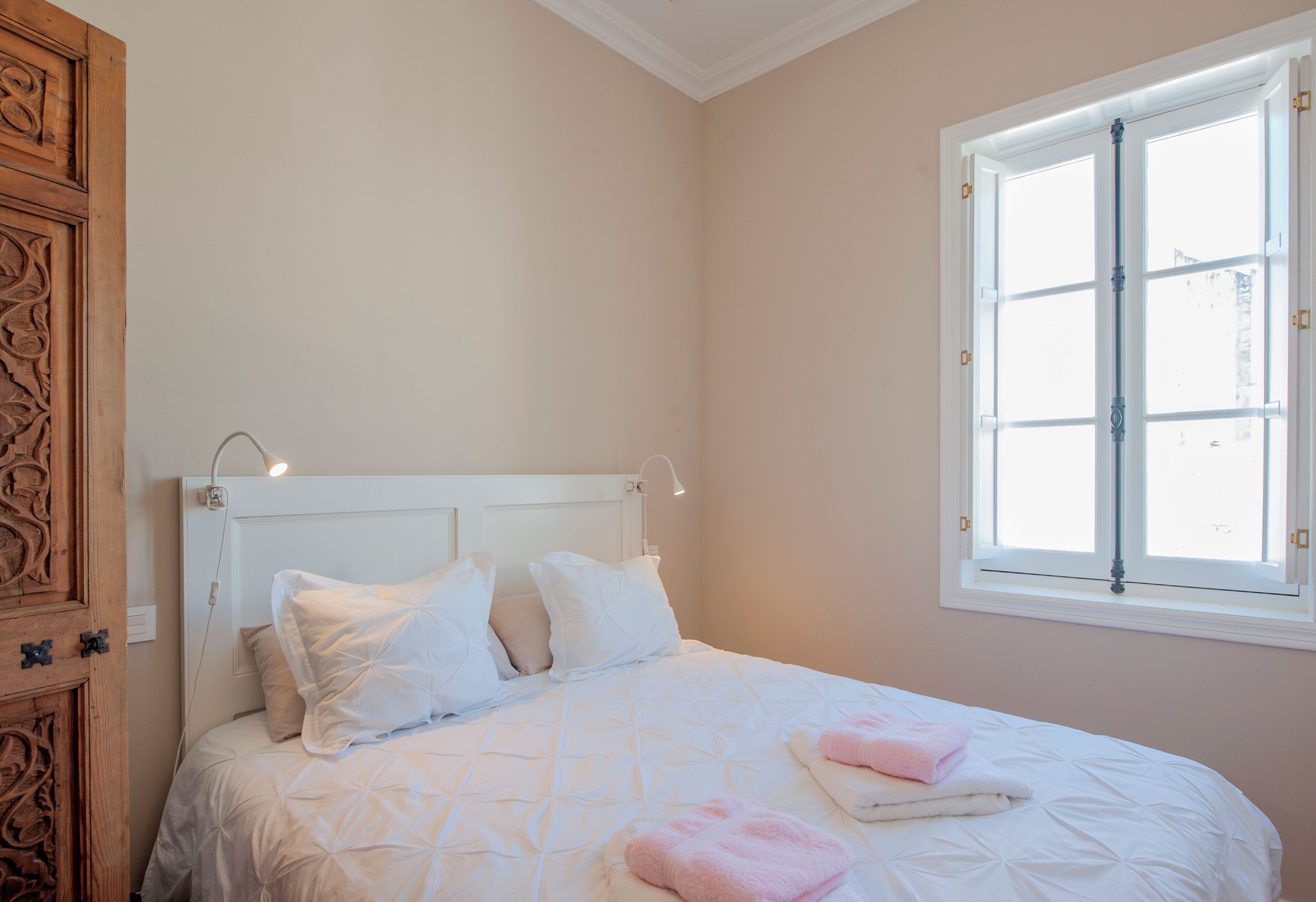 Un dormitorio con cama, almohadas, una ventana y un armario de madera.