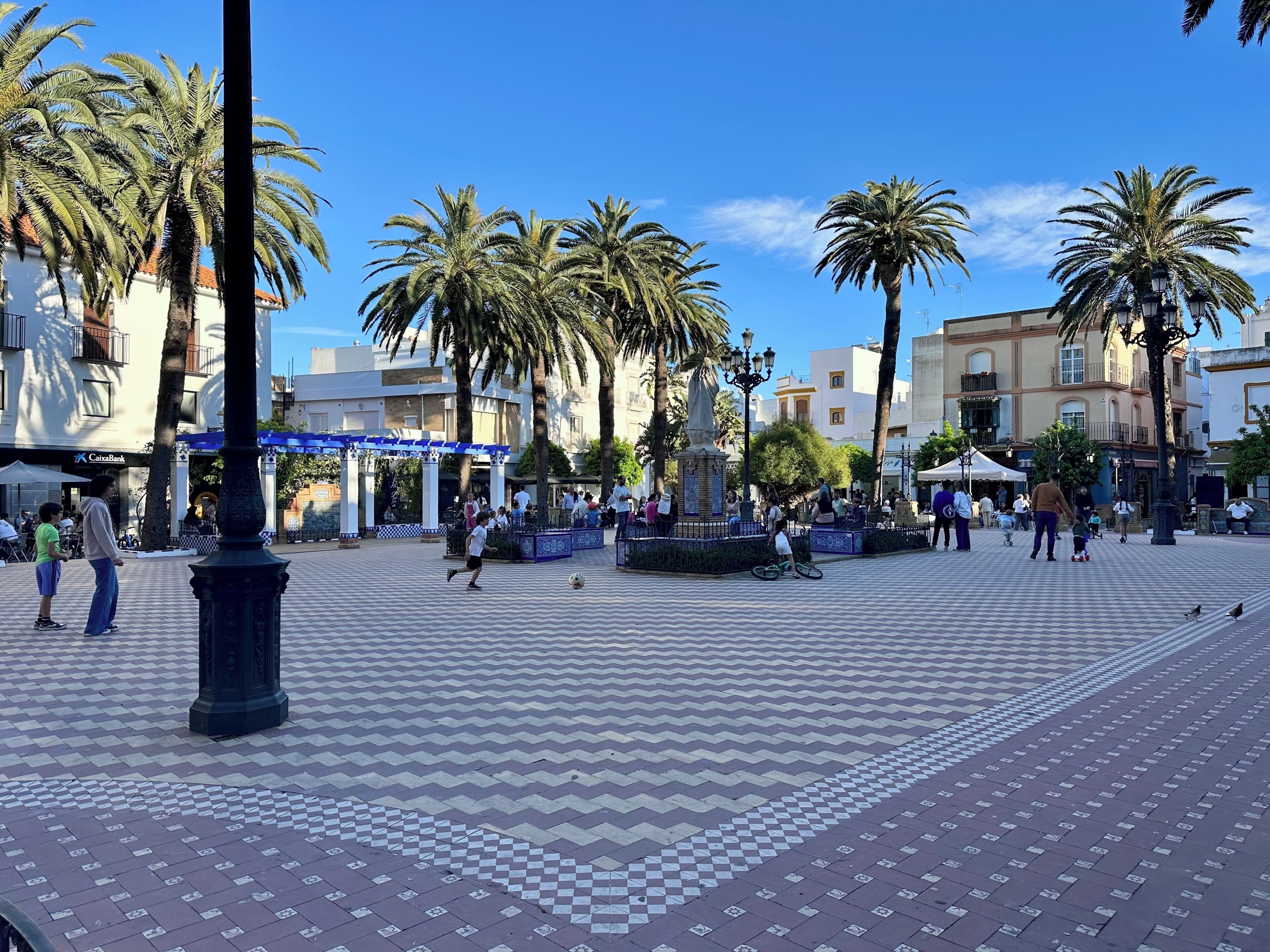 Una plaza pública con pavimento estampado, palmeras y gente.
