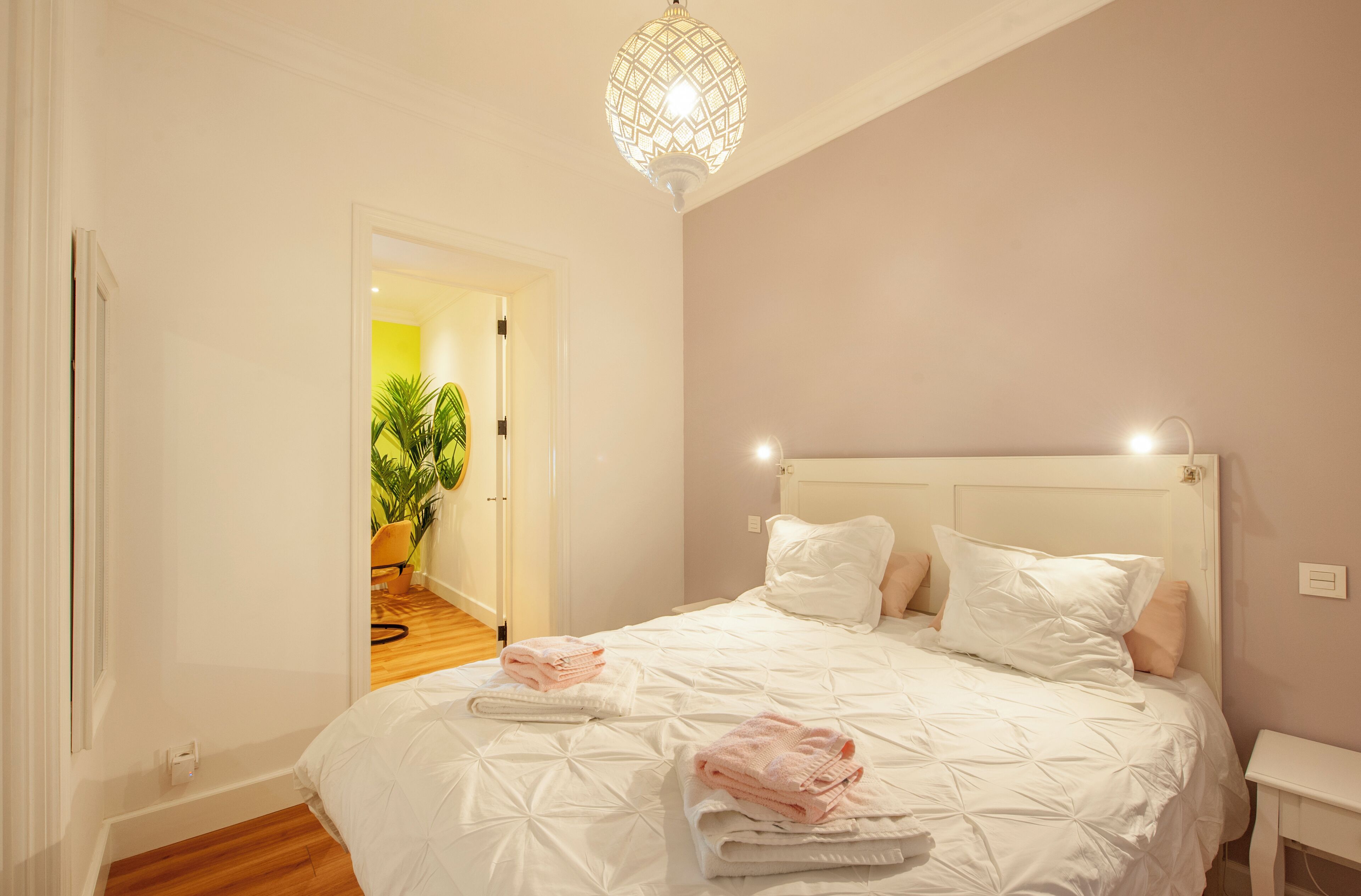 Ein Schlafzimmer mit einem großen Bett, weißer Bettwäsche, einem Nachttisch und einer Hängeleuchte.