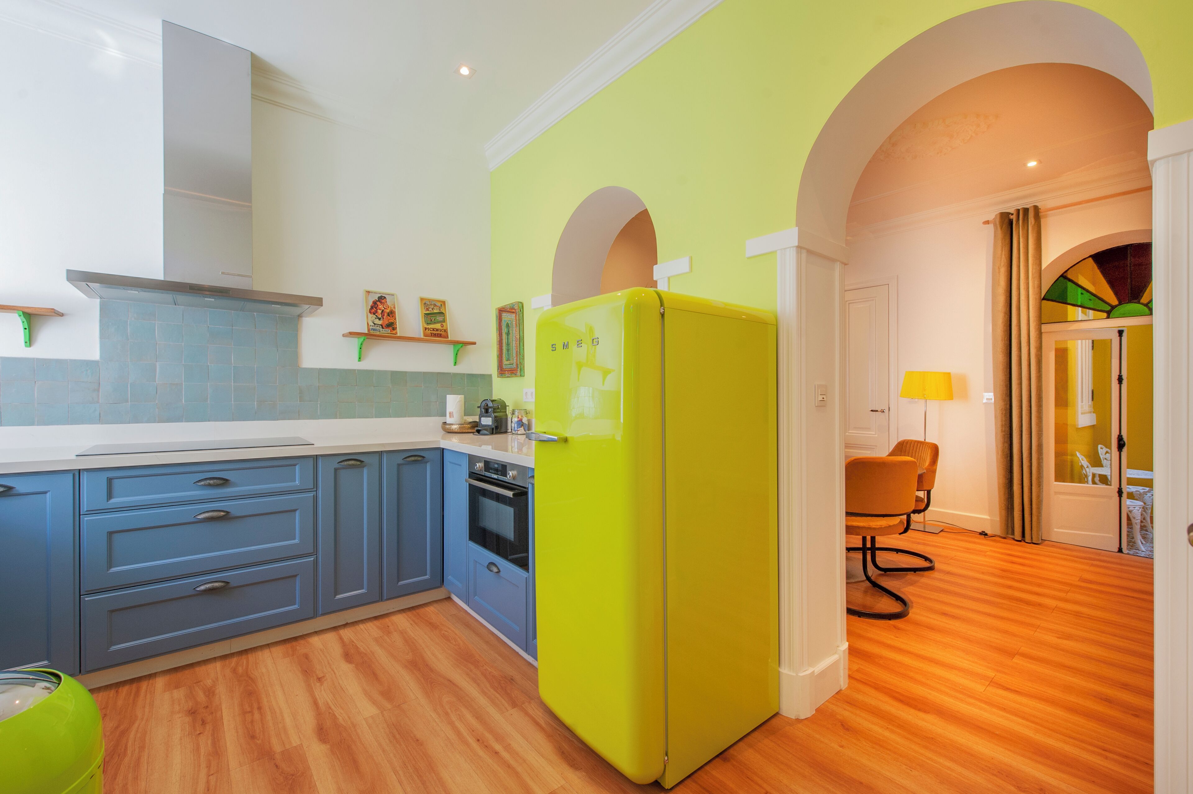 A kitchen with blue cabinets, a yellow refrigerator, and a wooden floor.