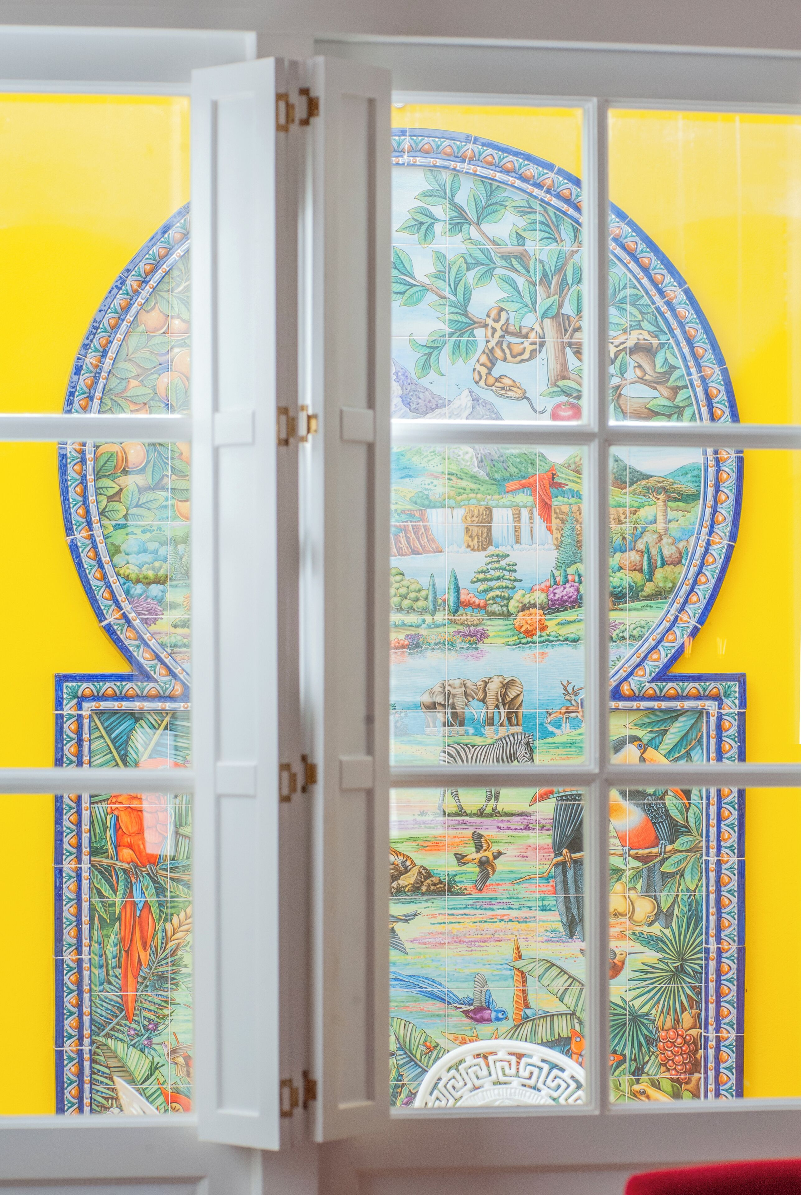A window with a colorful tropical scene, a white door frame, and a yellow wall.