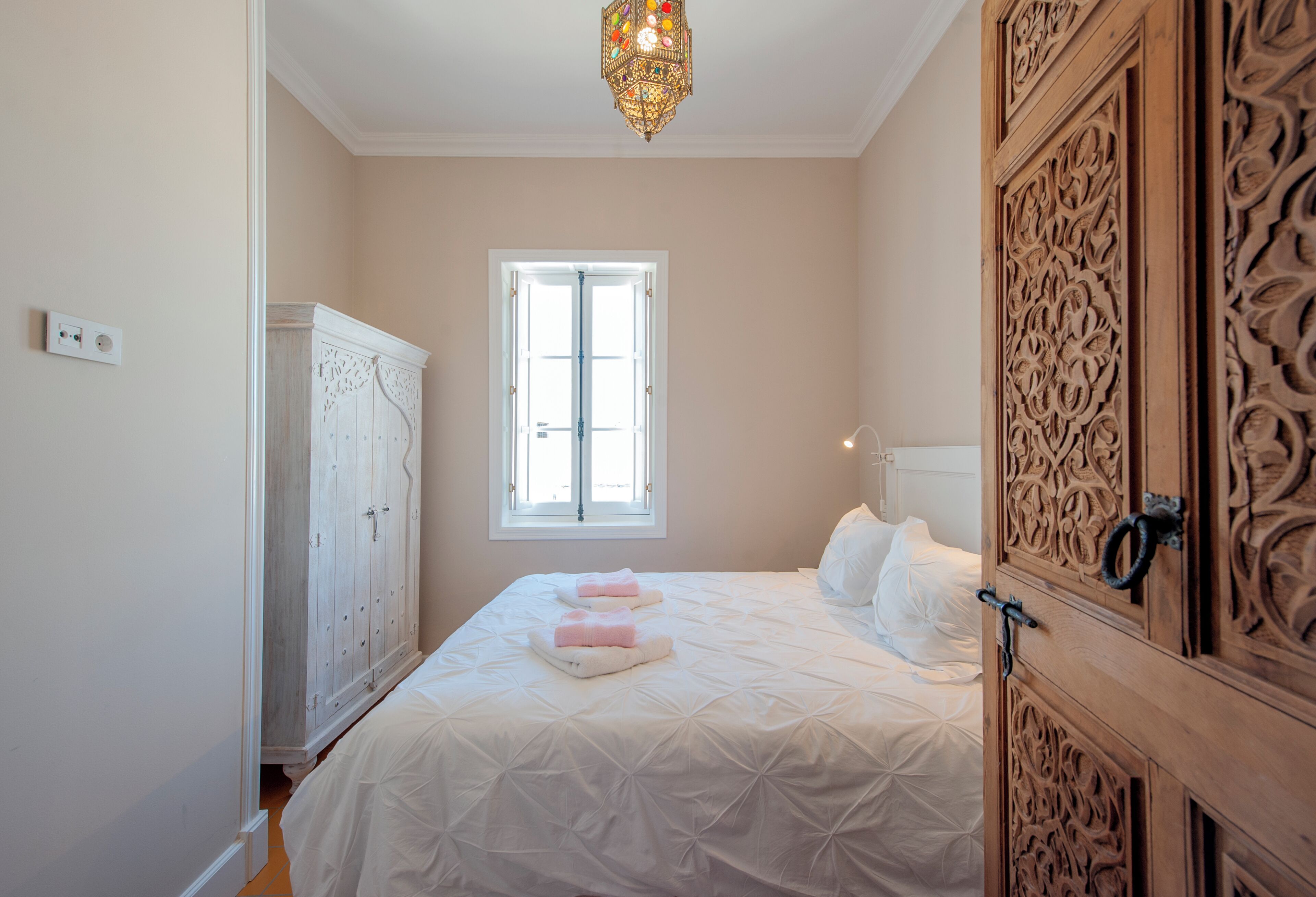 A bedroom with a bed, a wardrobe, a window, and a chandelier.