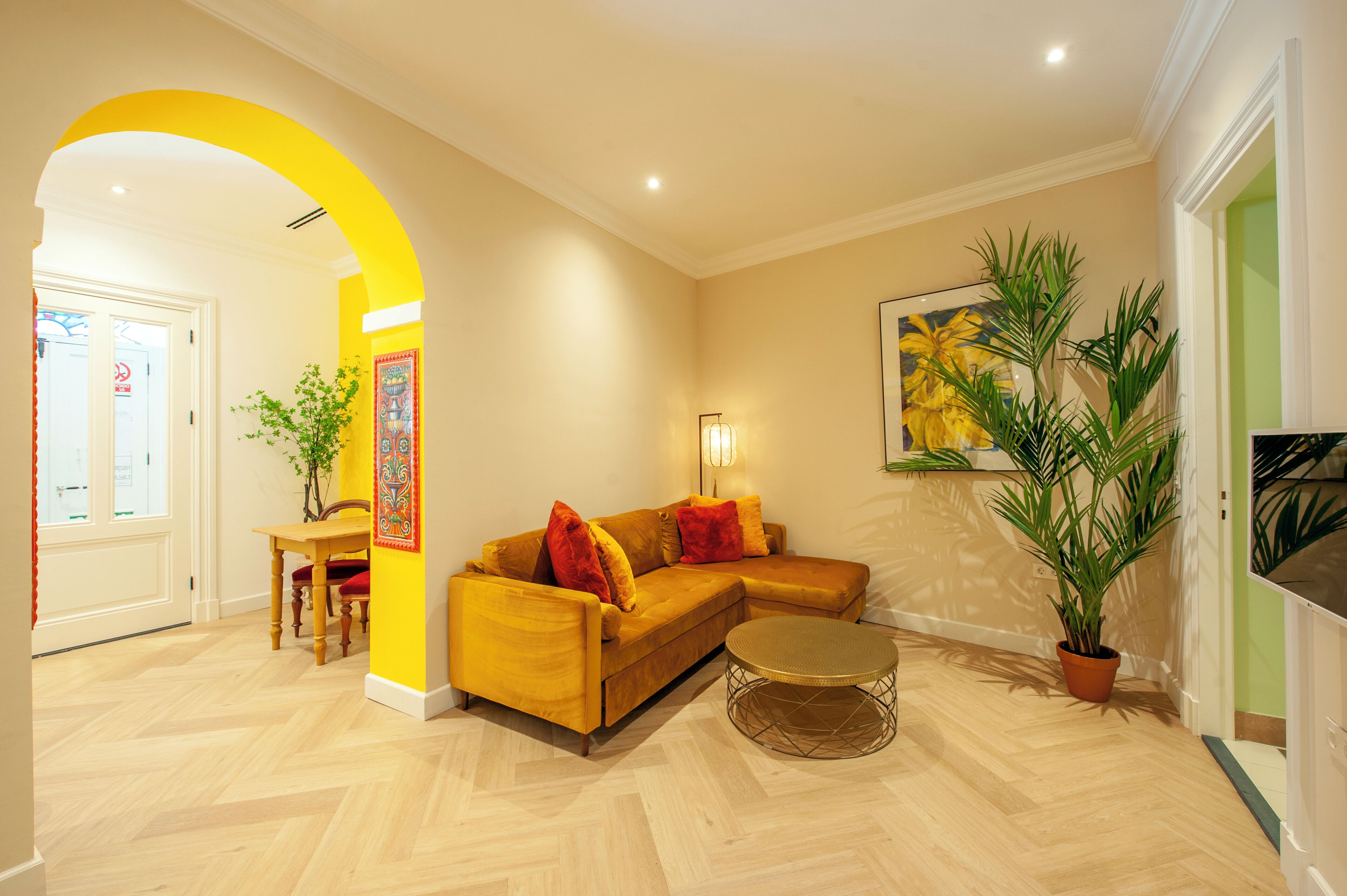 A living room with a yellow sofa, a round coffee table, and a large potted plant.