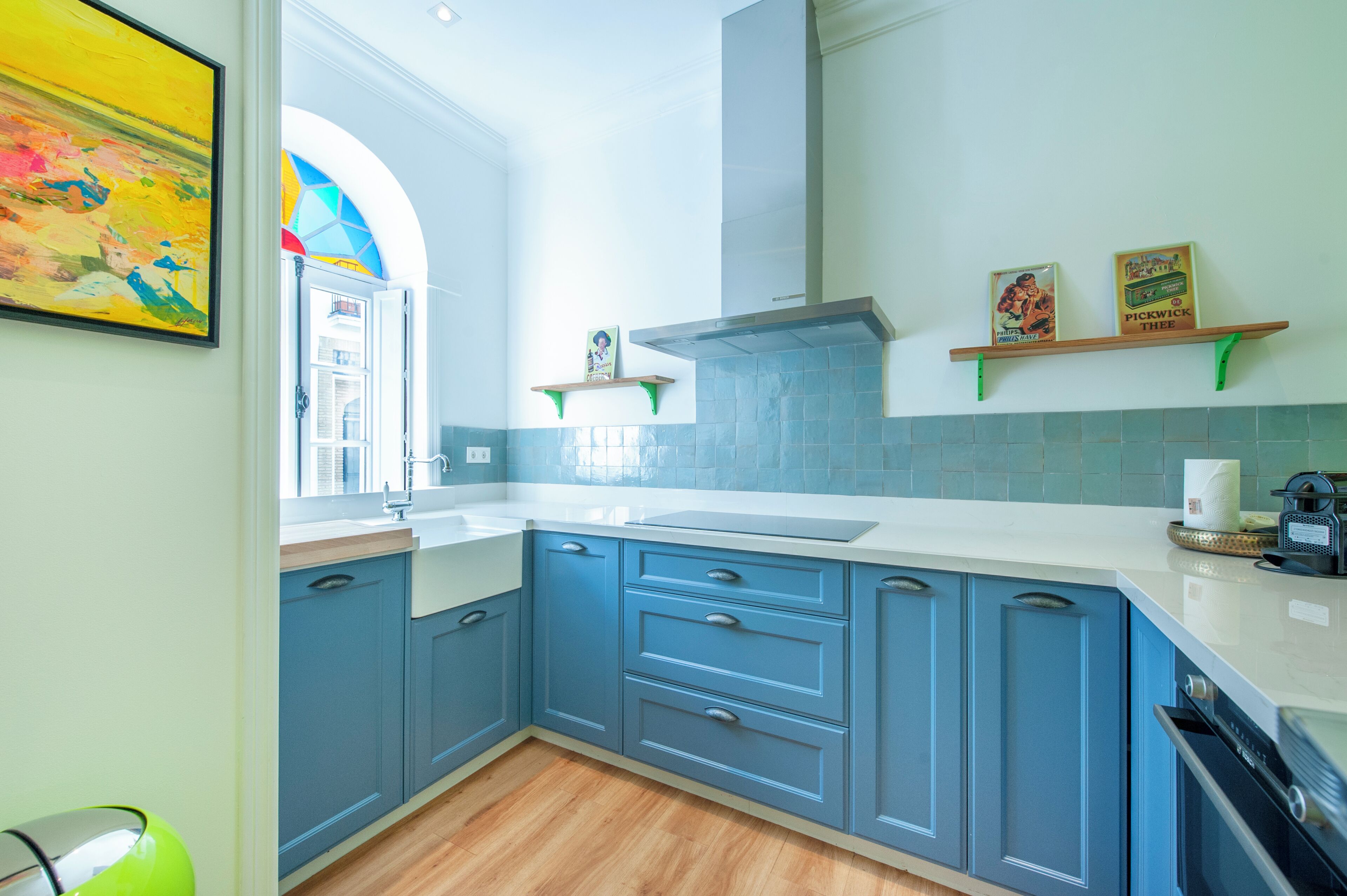 A modern kitchen with blue cabinets, a white countertop, and a large window.