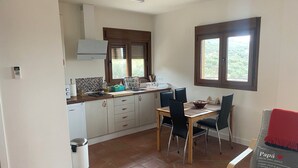 A compact kitchen with a dining area, featuring a tiled floor, a built-in oven, and a window with a view of greenery. - Villa Arriba (Periana)