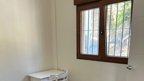 A small room with a white desk and chair, a window with bars, and a tiled floor. - Villa Arriba (Periana)