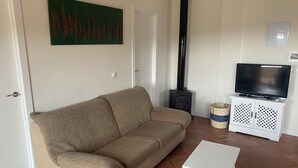 A living room with a beige sofa, a white TV stand, a small white table, and a decorative item on the floor. - Villa Arriba (Periana)