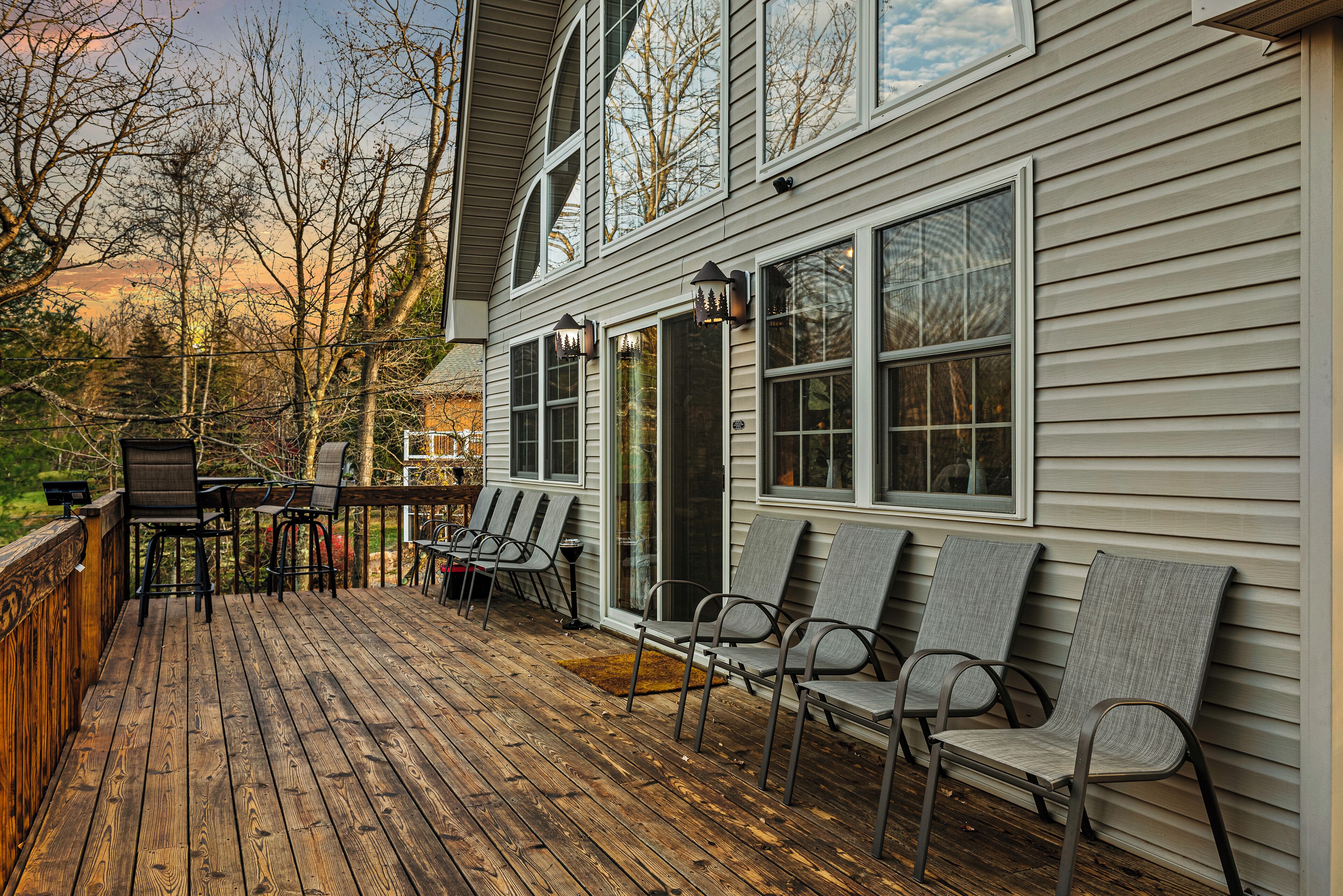 A wooden deck with outdoor seating and a view of a house with large windows and a covered porch.