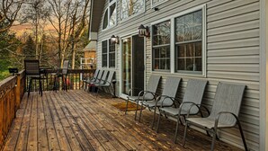 Un terrazzo in legno con posti a sedere all'aperto e vista su una casa con ampie finestre e un portico coperto.