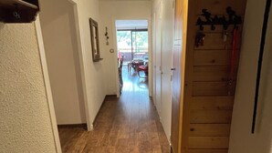A hallway with wooden flooring, a bench, a door, and a window leading to an outdoor area. - Chantemerle T2, 49m2, south-facing,   (Saint-Chaffrey)