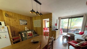 A cozy cabin interior with a wooden dining table, chairs, a sofa, and a large window offering a view of the outdoors. - Chantemerle T2, 49m2, south-facing,   (Saint-Chaffrey)