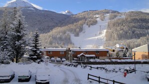 A snow-covered mountain landscape with a ski resort, including a building with a ski lift and a parking area with cars. - Chantemerle T2, 49m2, south-facing,   (Saint-Chaffrey)